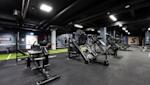 Moderne treningsstudio med svart treningsutstyr, grønne gulvdetaljer og industrielt tak med synlige rør og belysning.