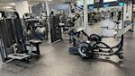 Modernt gym med svarta träningsredskap, roddmaskin i förgrunden och styrketräningsutrustning i ljust lokalt rum.