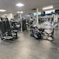 Modernt gym med svarta träningsredskap, roddmaskin i förgrunden och styrketräningsutrustning i ljust lokalt rum.