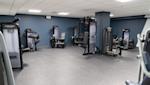 Modernt gym med svarta och grå träningsapparater mot mörkblå väggar, grått golv och vit takpanel med belysning.