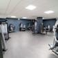 Modernt gym med svarta och grå träningsapparater mot mörkblå väggar, grått golv och vit takpanel med belysning.