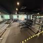 Modernt gym med hantlar, träningsbänkar och vikter. Svart tak, grått golv och stora fönster med grönska utanför.