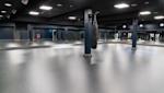 Rymligt gym med grått golv, svart tak, spegelväggar och en boxningssäck hängande från en blå pelare.