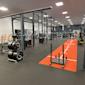 Modernt gym med power racks, viktskivor, orange träningsmatta och träningsutrustning i ett välupplyst lokalt.