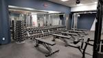 Modernt gym med blå väggar, träningsbänkar, hantlar i ställ och träningsutrustning under vitt takpaneltak.