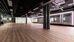 Moderne hotstudio med tregulv, svart tak, søyler og store speil med LED-belysning langs veggene.