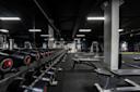 Moderne treningsstudio med rekke svarte manualer med røde detaljer, treningsbenker og apparater i mørkt rom med hvit belysning.