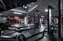 Moderne treningsstudio med romaskiner i forgrunnen, styrkeapparater og boksering i bakgrunnen, industrielt tak.