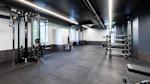 Moderne treningsstudio med svart tak, hvite vegger, grått gulv og treningsutstyr som kabelmaskin og vektstativ.