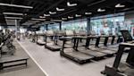 Modernt gym med rad av svarta löpband, styrketräningsutrustning och stora fönster under industriellt svart tak.