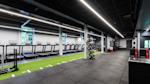 Moderne treningsstudio med tredemøller langs veggen, grønn løpebane på gulvet og svart tak med LED-belysning.