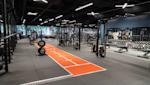 Modernt gym med svart tak, orange löpbana, träningsutrustning och hantlar längs väggarna med LED-belysning.