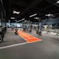 Modernt gym med svart tak, orange löpbana, träningsutrustning och hantlar längs väggarna med LED-belysning.