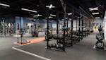 Modernt gym med svart utrustning, orange träningsområde och exponerat svart tak med industriell belysning.