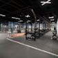 Modernt gym med svart utrustning, orange träningsområde och exponerat svart tak med industriell belysning.