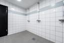 Moderne dusjerom med hvite fliser, blå mosaikk-stripe, to dusjhoder og grått gulv med sluk.