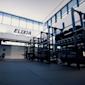 Moderni kuntosali, jossa ELIXIA-logo seinällä, mustia voimailutelineitä ja painoja, suuret ikkunat.
