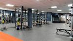 Modernt gym med svarta träningsställningar, färgglada viktskivor och grått golv med orange detalj.