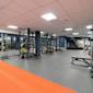 Modernt gym med svarta träningsställningar, färgglada viktskivor och grått golv med orange detalj.