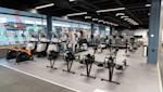 Modernt gym med roddmaskiner och motionscyklar, svart tak med LED-belysning och stora fönster mot gatan.