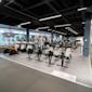 Modernt gym med roddmaskiner och motionscyklar, svart tak med LED-belysning och stora fönster mot gatan.