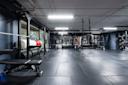 Moderne treningsstudio med grått gulv, svarte vegger, treningsutstyr og vekter, opplyst av hvite taklys.
