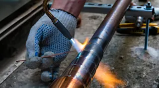 Construction worker welding copper pipe.