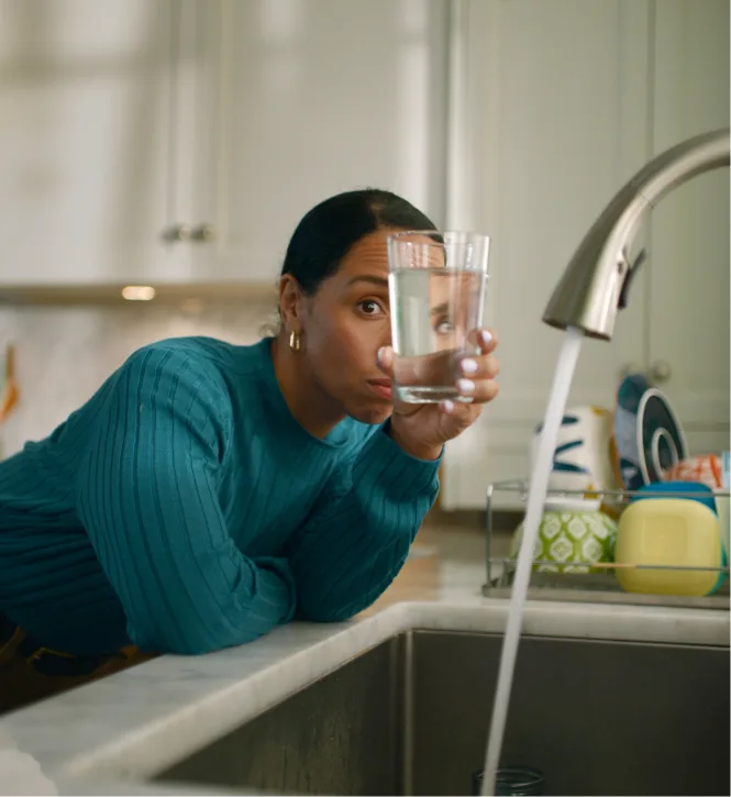 Woman examining the water in her glass after having filled it from her kitchen faucet with tap water.