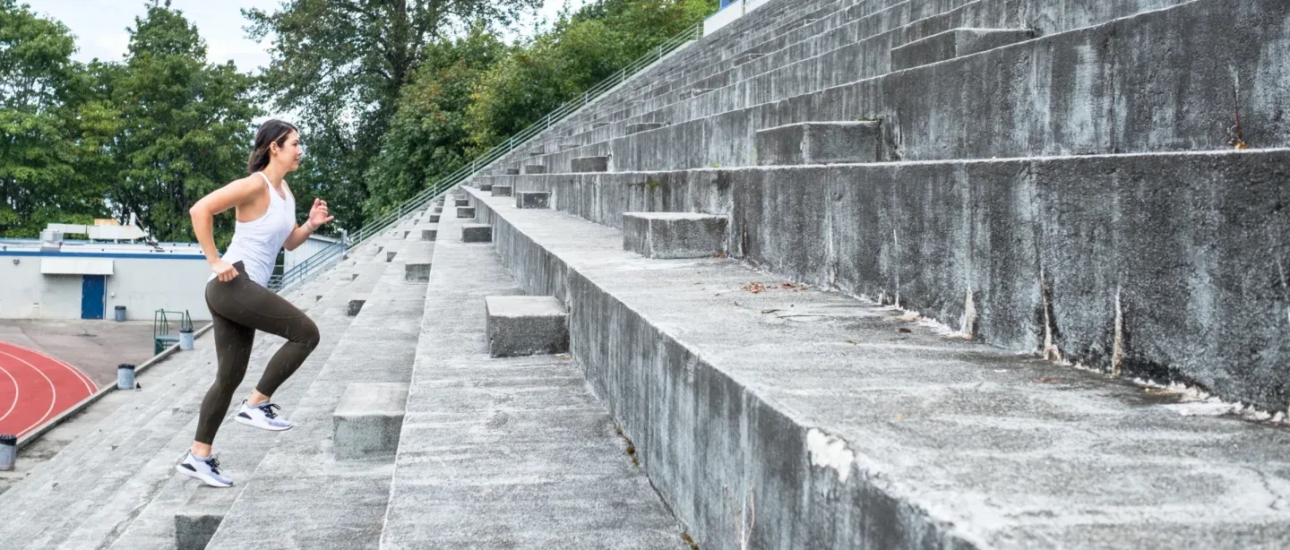 Woman in workout attire running up stadium steps.