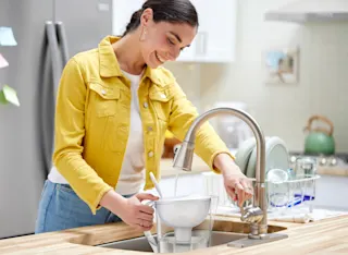 Woman filling up white Brita pitcher in kitchen sink.