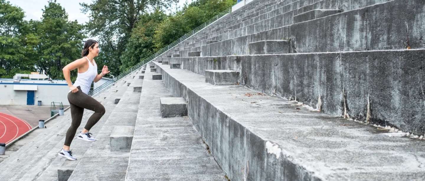 Woman in workout attire running up stadium steps.