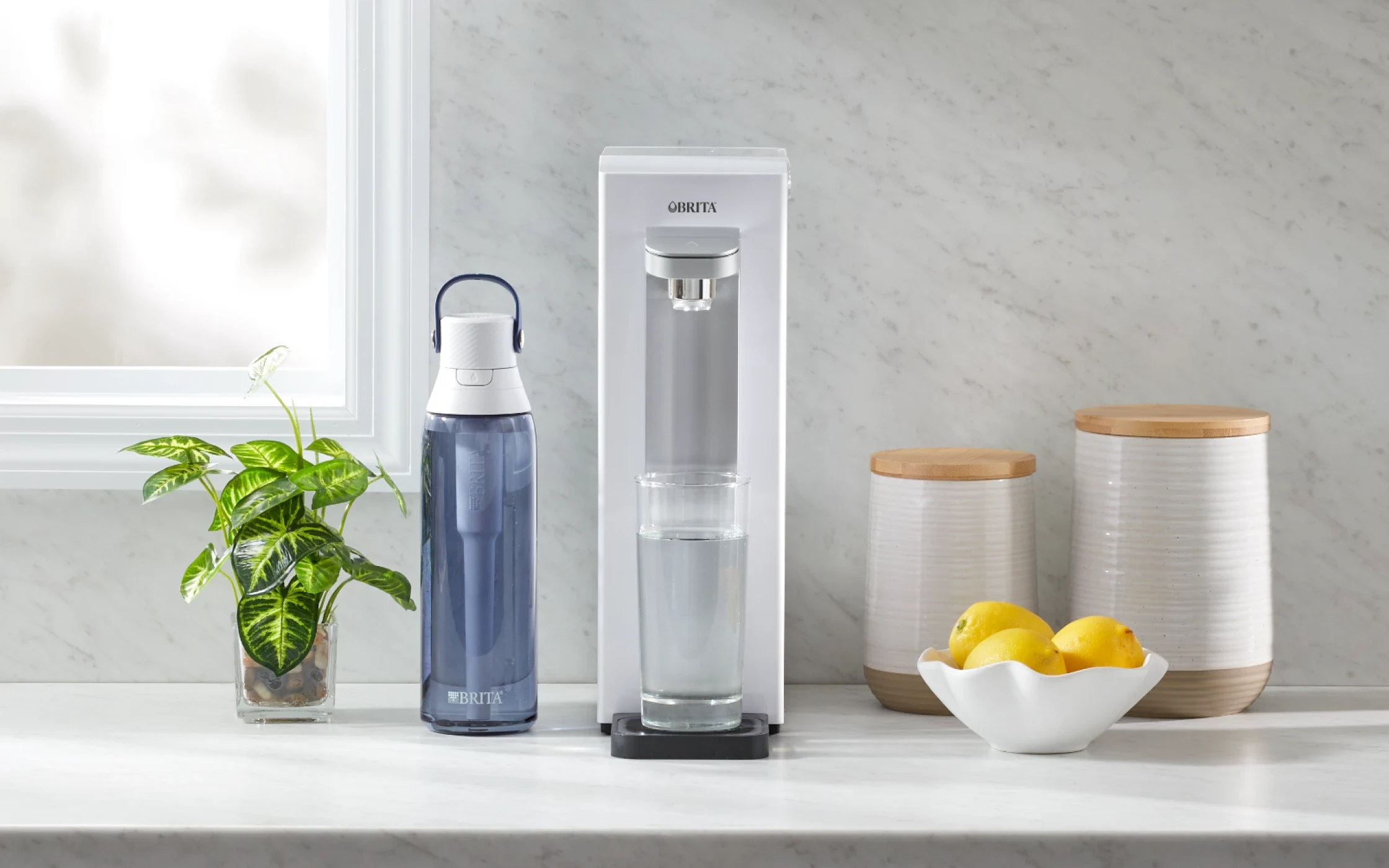 Grey Brita Hub™ Compact Countertop Water Filter System on kitchen counter next to Brita water bottle.