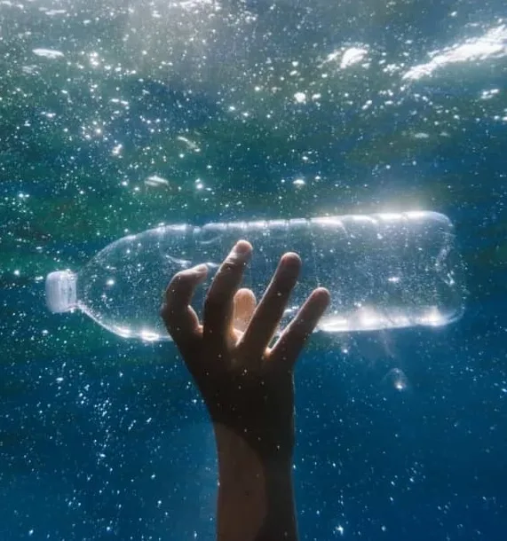 Hand holding empty water bottle under water.
