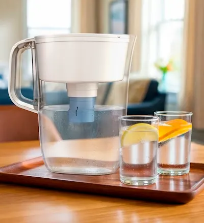 Brita pitcher with Elite filter on wooden tray on top of table with two glasses of water with orange slices in them.