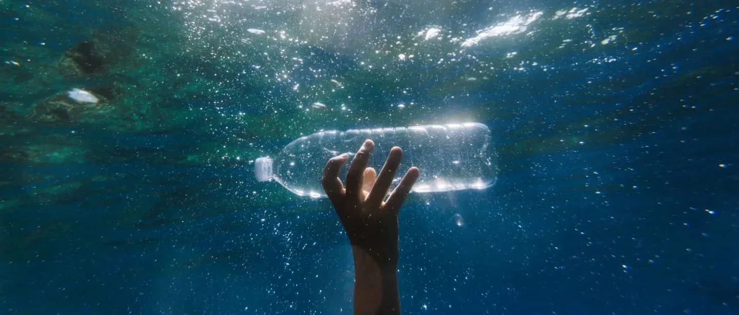 Hand holding empty water bottle under water.