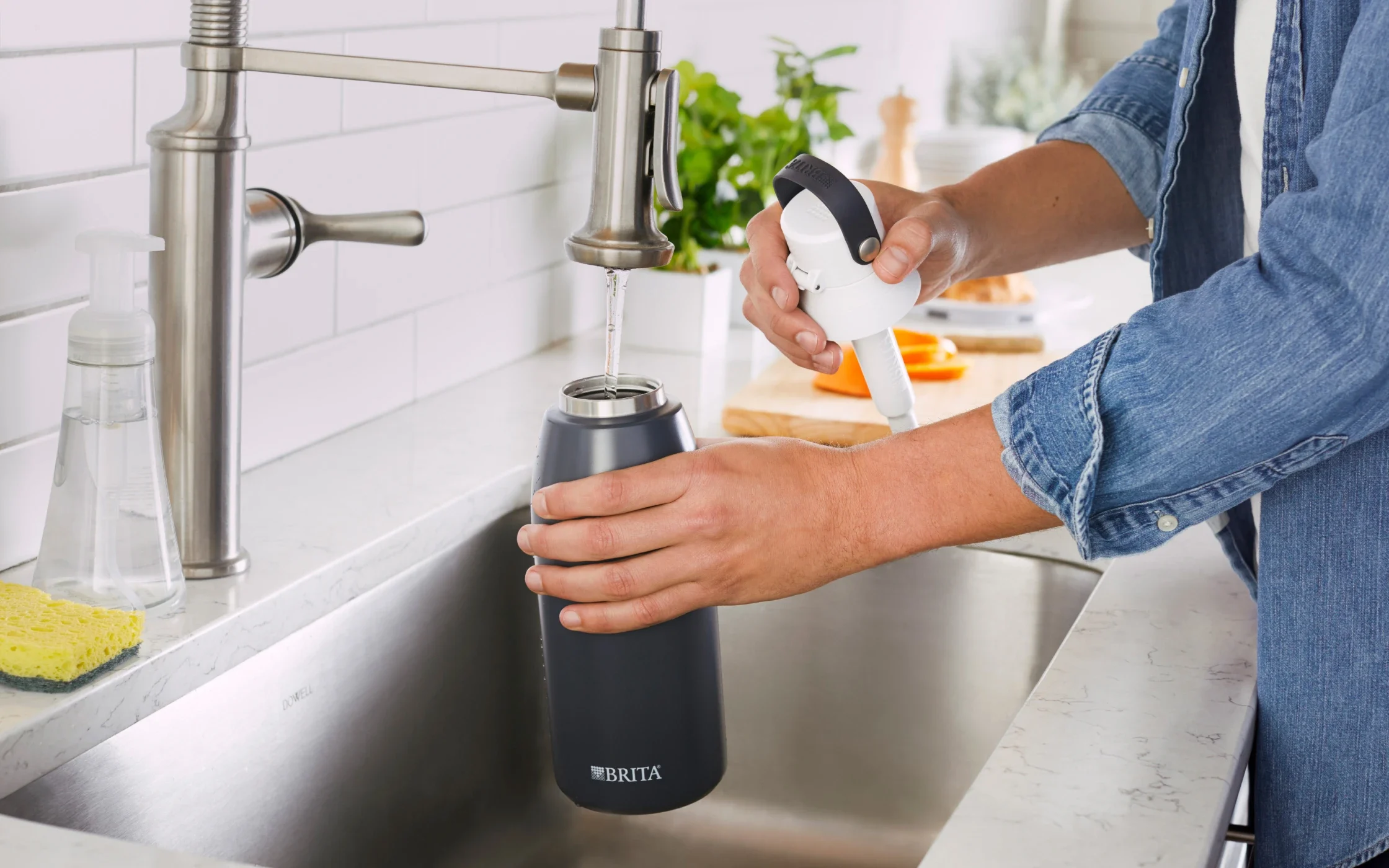 Person filling their Carbon, Stainless Steel, 32oz Brita water bottle with tap water from the sink.