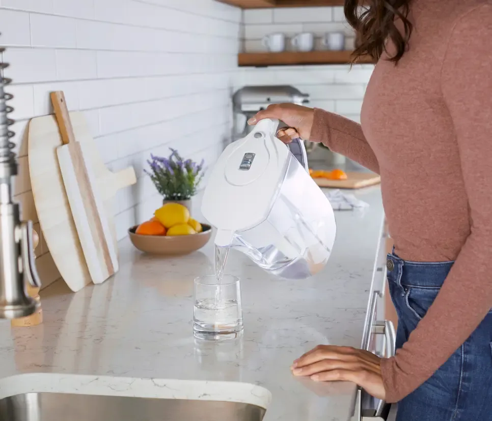 Woman filling her water glass on kitchen counter with white Brita pitcher.