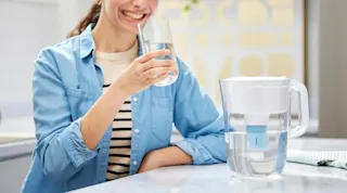 Girl sitting in kitchen holding a glass of water, with Brita pitcher with elite filter next to her.