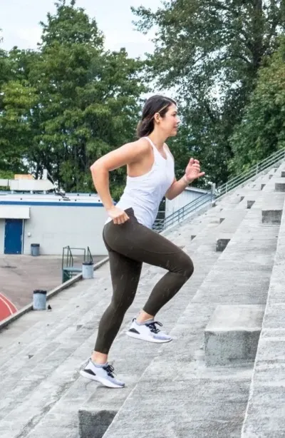 Woman in workout attire running up stadium steps.