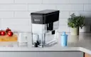 Black Ultramax Water Dispenser with Elite Filter on kitchen counter next to water glass.
