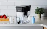 Black Ultramax Water Dispenser with Elite Filter on kitchen counter next to water glass.