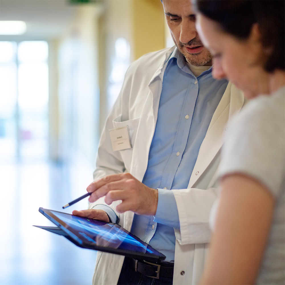 A doctor discusses a diagnosis with a patient using a tablet. The 5G network enables real-time networking and thus helps patients.