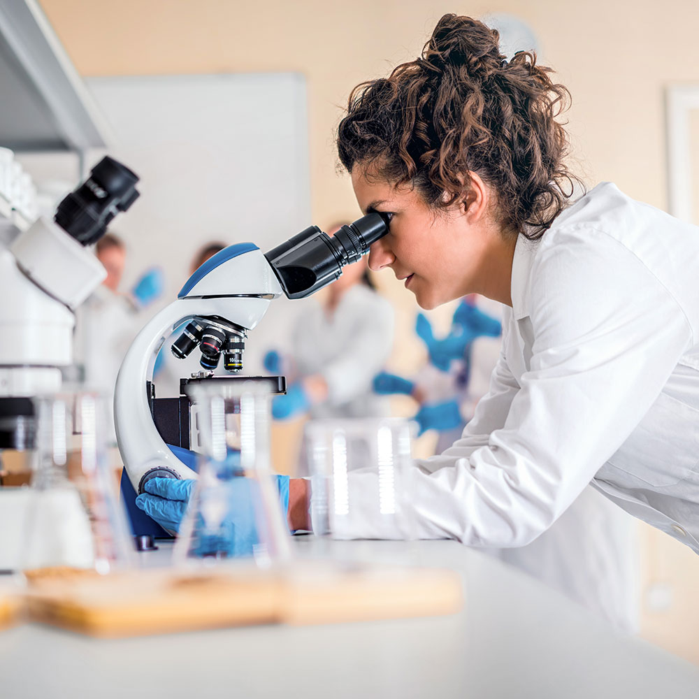 A woman in a white coat is looking through a microscope. The fear of electromagnetic fields and DNA damage makes people distrust mobile communications. We present studies that show that fear and mistrust are unfounded.