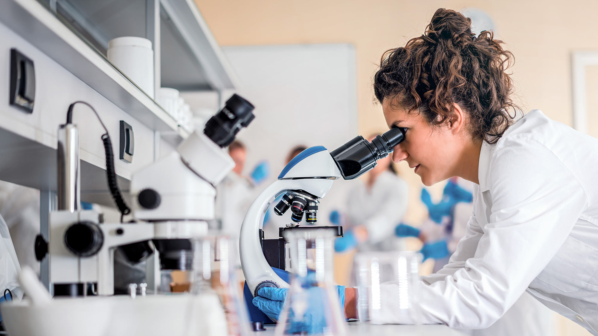 Frau in weißem Kittel schaut durch ein Mikroskop. Die Angst vor elektromagnetischen Feldern und einer Schädigung der DNA lässt Menschen dem Mobilfunk misstrauen. Hier stellen wir Studien vor, die zeigen, dass Angst und Misstrauen unbegründet sind.