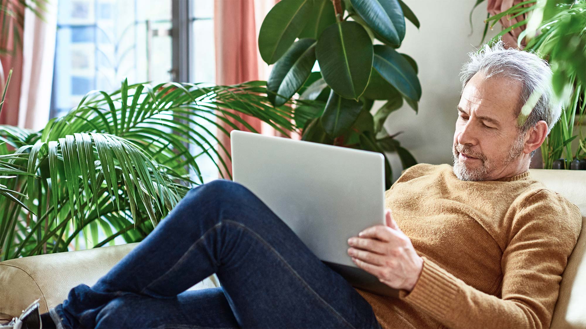 A man in a sweater is sitting on a sofa in front of indoor plants and is reading on his laptop. Many people are concerned that the new mobile communications standard carries health risks. We clarify and show reassuring scientific evidence.