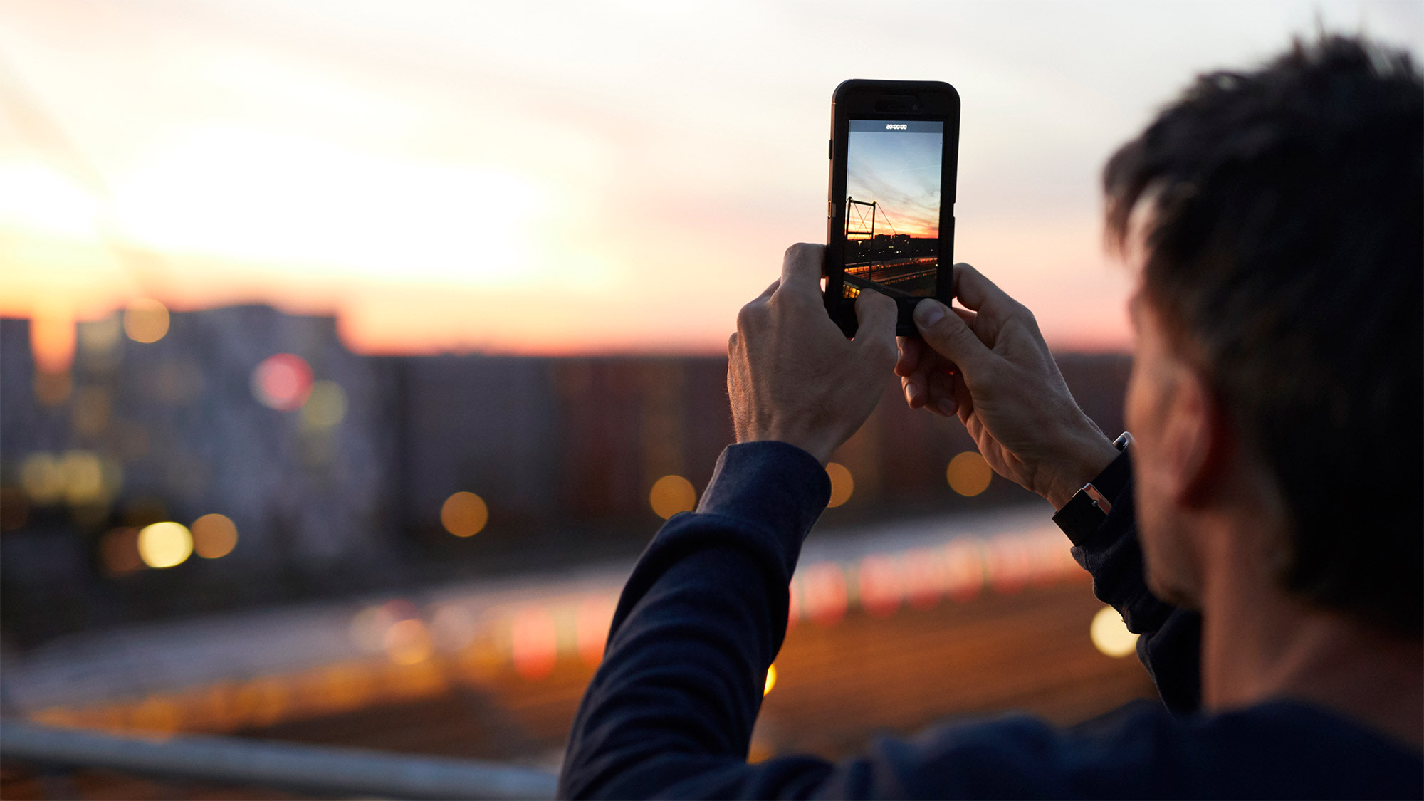 Mann steht auf einer Brücke und fotografiert den Sonnenuntergang über einem Gleisbett. Der Strahlenschutz hat bei 5G oberste Priorität. 
