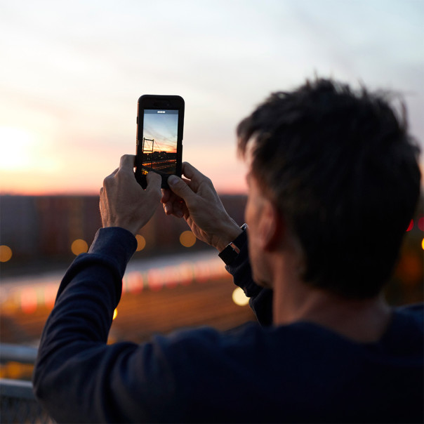 Mann steht auf einer Brücke und fotografiert den Sonnenuntergang über einem Gleisbett. Der Strahlenschutz hat bei 5G oberste Priorität. 
