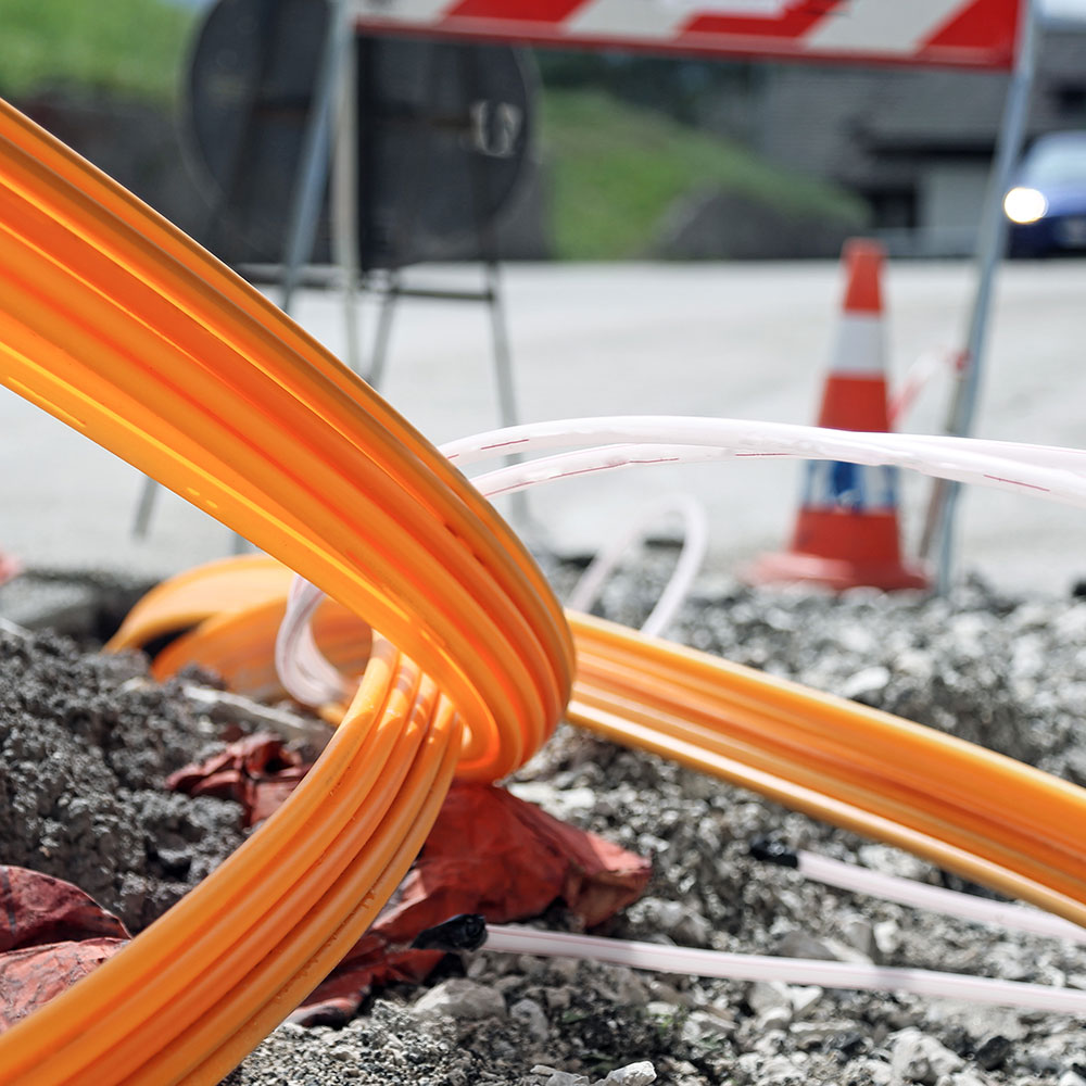 Glasfaserkabel ragen aus Baustelle auf einer Straße. Glasfaserleitungen sind die beste Möglichkeit, um das 5G-Netz zum Sendemast zu bringen. 