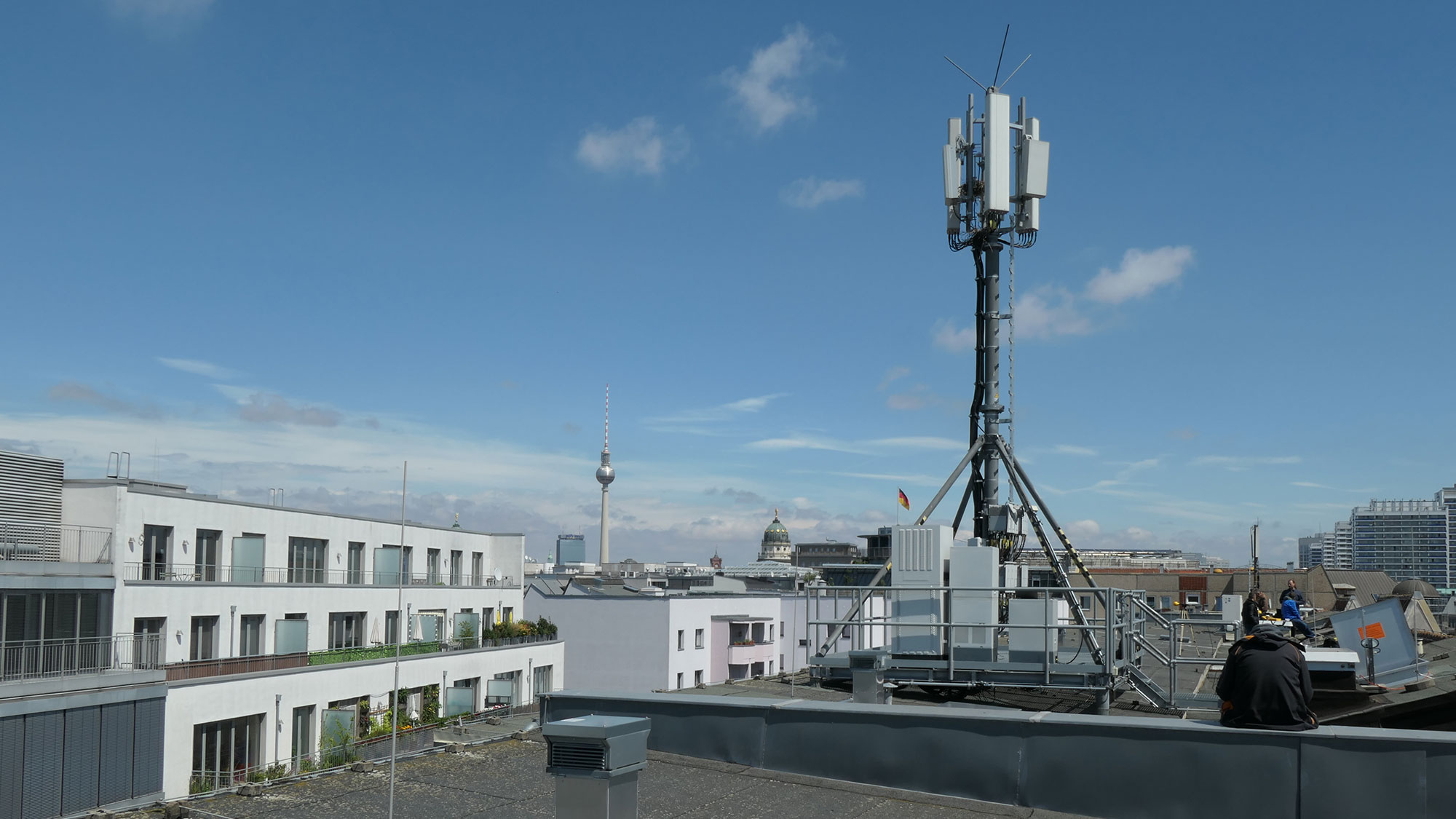 Mobilfunkmast ragt in den blauen Himmel über den Dächern von Berlin.