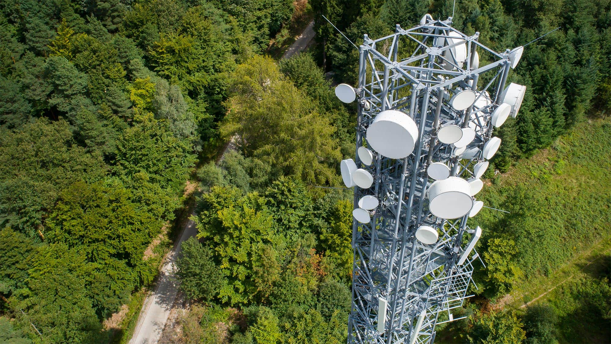 Bird's eye view of a transmission tower in front of a forest. New transmission towers are being built for the 5G network. However, the proximity to them and the electromagnetic fields is not dangerous. 